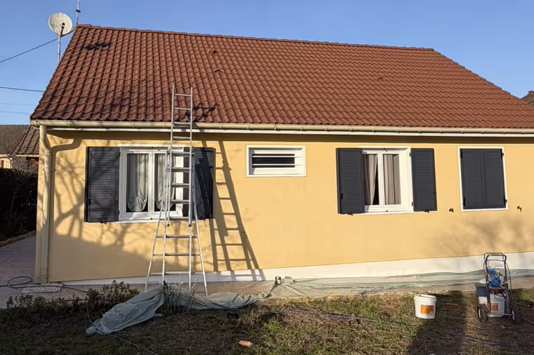 Traitement hydrofuge de toiture en cours sur une maison, tuiles rouges, échelle et pulvérisateur au sol