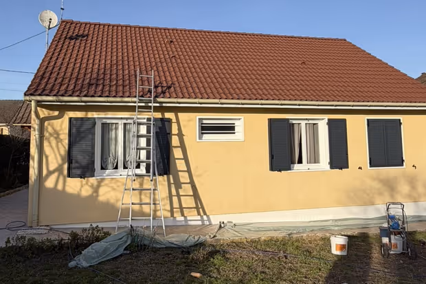 Traitement hydrofuge de toiture en cours sur une maison, tuiles rouges, échelle et pulvérisateur au sol