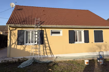 Traitement hydrofuge de toiture en cours sur une maison, tuiles rouges, échelle et pulvérisateur au sol